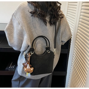 Detail of black matte bucket bag with star and bear charms on gray knit outfit