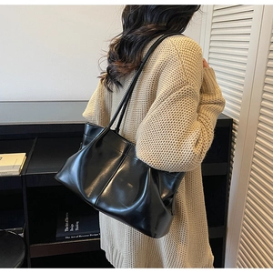 Model wearing black pleated tote bag with glossy finish in a modern home setting
