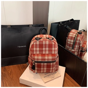 Close-up of the red tartan backpack featuring black leather handle and zipper detail