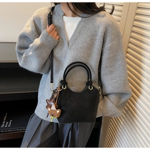 Detail of black faux leather bucket bag with woven handle and plush bear charm on model