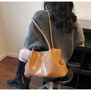 Detail showing pleated caramel leather shoulder bag texture and spacious capacity on model