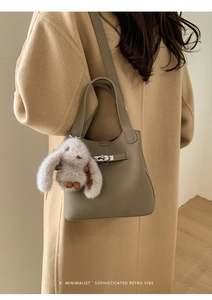 Detail view of taupe leather bucket bag with silver twist lock and plush rabbit charm