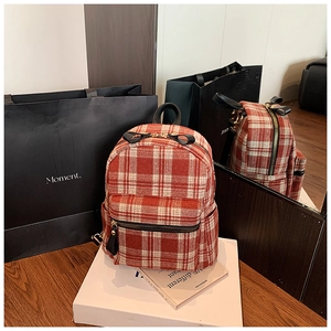 Detail of red and white plaid tweed backpack featuring a black bow zipper and multi-pockets