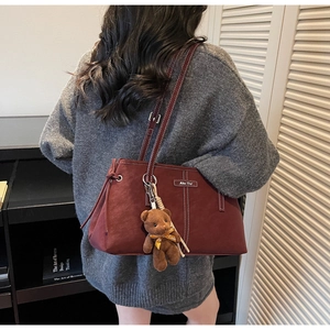 Detail of burgundy tote bag with white contrast stitching and a plush bear charm
