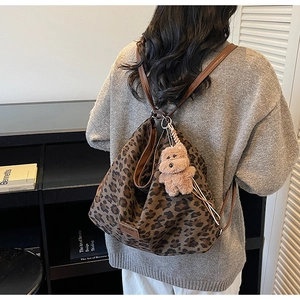 Detail of leopard print tote bag with brown leather straps and plush bear charm