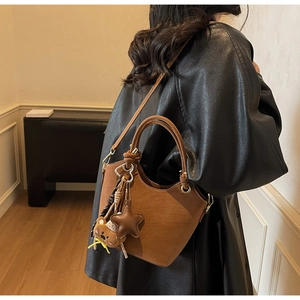 Brown retro bucket bag with teddy bear charm shown in a warm indoor lifestyle setting