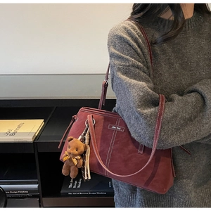 Detail of burgundy tote bag with brown bear charm pendant on model's shoulder