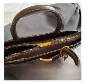 Detail of dark brown leather handbag with gold zipper hardware and plush ball charm