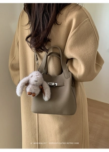 Detail of taupe lychee leather bucket bag with metal buckle and plush bunny charm
