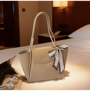 Detail of beige pebbled leather tote bag with gold buckle and decorative patterned silk scarf