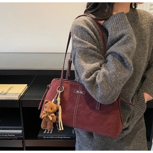 Detail of burgundy tote bag with white stitching and cute brown bear pendant on a model