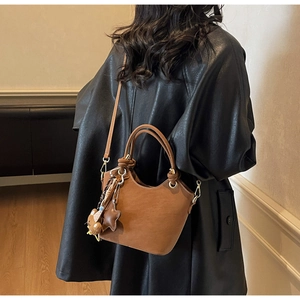Brown leather bucket bag styled as a crossbody on a person with cute charms