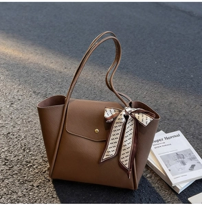 Close-up of brown pebbled leather tote bag featuring golden buckle and silk scarf detail
