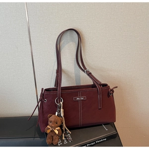 Detail of burgundy shoulder bag with white contrast stitching and brown teddy bear charm