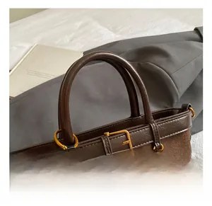 Detailed close-up of brown suede handbag featuring gold buckle and plush pom-pom charm