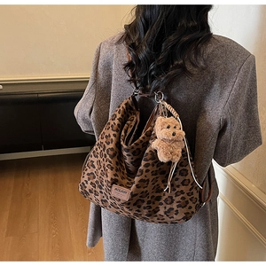 Detail of leopard print tote bag with plush bear charm in a soft home interior setting