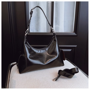 Detail view of glossy black faux leather shoulder bag with side flap pockets and silver hardware