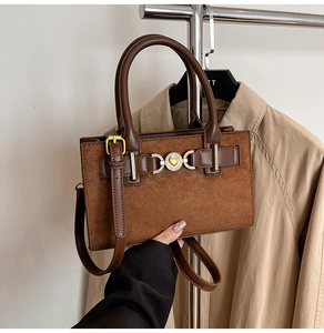 Detail of a brown patchwork handbag featuring a golden heart buckle and slim crossbody strap