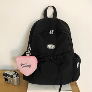 Detail eines schwarzen Nylon-Rucksacks mit dekorativer Schleife und rosa Herzanhänger