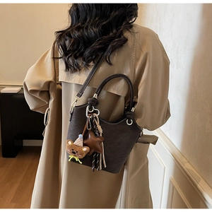 Brown suede crossbody bag with plush bear charm styled on a khaki trench coat back view