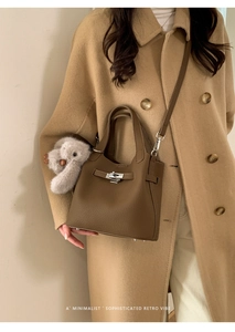 Detail of a brown leather bucket bag with silver lock and plush bunny charm on a coat