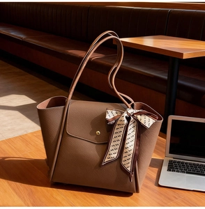 Close-up of brown pebbled leather tote bag with gold metal clasp and decorative silk scarf