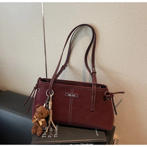 Close-up of wine red tote bag with contrast stitching and brown teddy bear charm