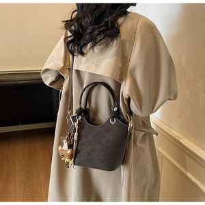 Close-up of a brown suede bucket bag with a cute bear charm on a model in a trench coat
