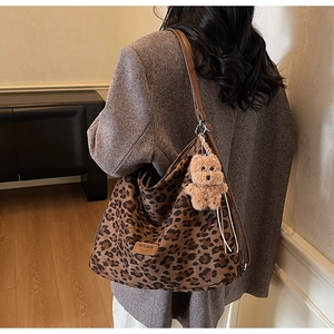 Detail of leopard print tote bag with brown leather straps and a plush bear charm pendant