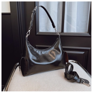 Detail showing the glossy leather texture and adjustable strap of the black crescent bag