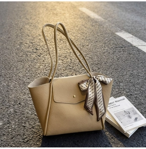 Detail view of beige lychee leather tote bag with silk scarf on a natural street surface