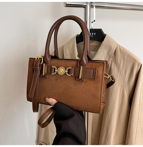 Detail of a brown leather shoulder bag with a gold heart buckle and crossbody strap