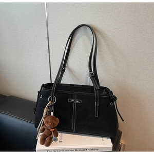 Detail of matte black tote bag with white contrast stitching and plush bear charm