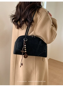 Close-up of black matte suede shoulder bag with retro wooden bead tassel on a model