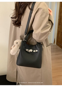 Detail of black lychee grain bucket bag with silver buckle and plush doll charm
