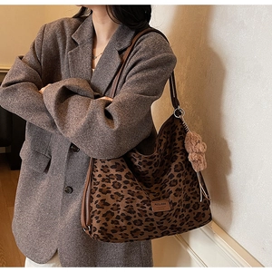 Detail of leopard print tote bag with brown leather straps and plush bear charm