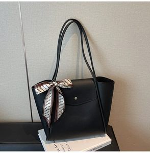 Close-up of a black leather tote bag with silk scarf detail and gold magnetic buckle