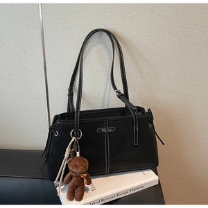 Close-up of black matte tote bag with contrast stitching and bear charm on art books