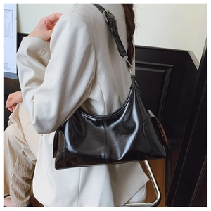 Detail of black glossy hobo bag featuring side flap pockets and adjustable shoulder strap
