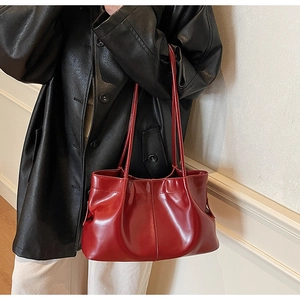 Side view of red pleated faux leather tote bag showing drape and texture on shoulder
