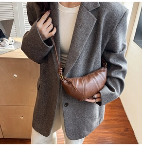 Brown leather croissant bag with segmented stitching shown on a person wearing a grey blazer
