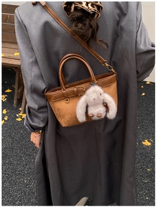 Rear view of model holding a brown suede and leather bucket bag with a rabbit charm