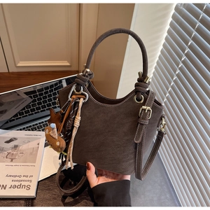 Detail of dark brown suede bucket bag with teddy bear charm and knotted handle