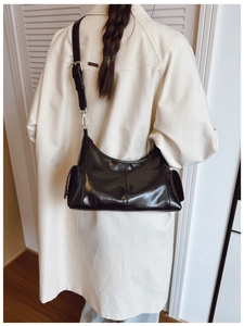 Detail of minimalist black glossy leather shoulder bag with side pockets and silver buckles