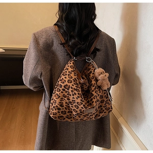 Detail of leopard print hobo bag with plush bear charm worn by a model in soft light