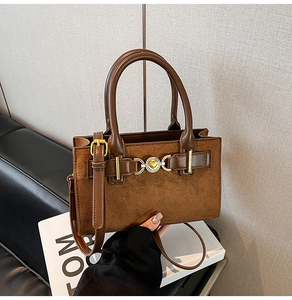 Close-up of brown suede handbag with golden heart buckle and smooth leather handles