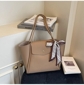 Close-up of beige tote bag with litchi texture, gold buckle and patterned silk scarf