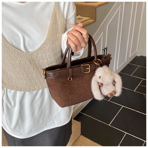 Detail of dark brown suede bucket bag with metal buckle and plush bunny charm