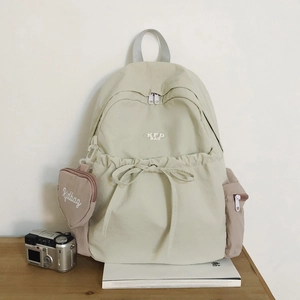 Detail eines cremefarbenen Nylon-Rucksacks mit schicker Schleife und Herz-Geldbörsen-Anhänger