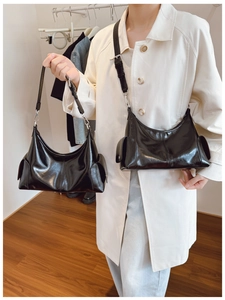 Detail of glossy black hobo bag with side pockets and silver buckles on a beige trench coat